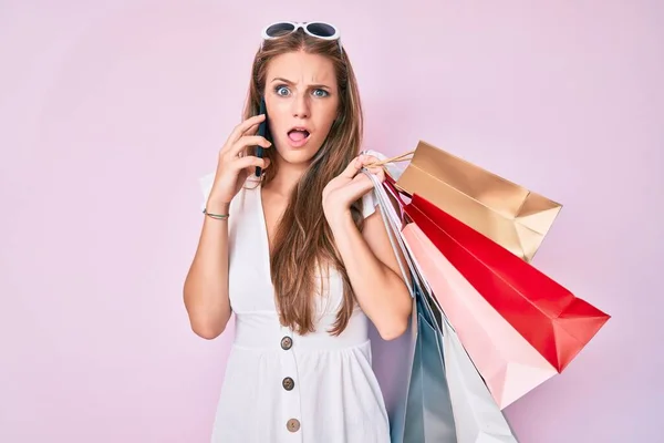 Jovem Loira Segurando Sacos Compras Falando Smartphone Face Choque Parecendo — Fotografia de Stock