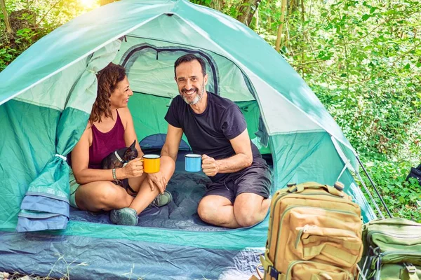 Middle age couple  of hiker smiling happy looking at the camera. Drinking coffee camping at the forest.