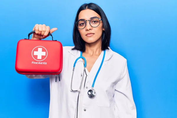 Young beautiful latin woman wearing doctor stethoscope holding first aid kit thinking attitude and sober expression looking self confident