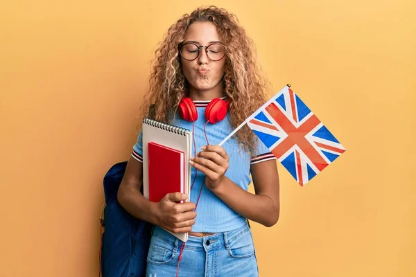 Beautiful caucasian teenager girl exchange student holding uk flag looking at the camera blowing a kiss being lovely and sexy. love expression.