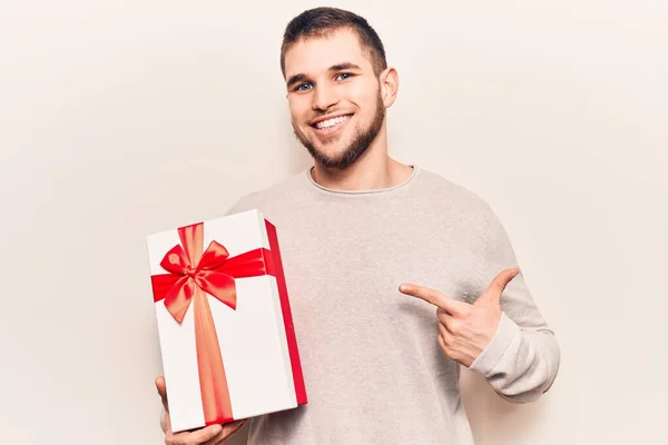 Jovem Homem Bonito Segurando Presente Sorrindo Feliz Apontando Com Mão — Fotografia de Stock