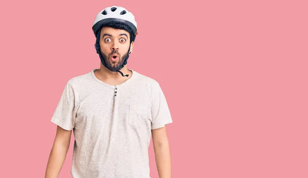 Young hispanic man wearing bike helmet scared and amazed with open mouth for surprise, disbelief face
