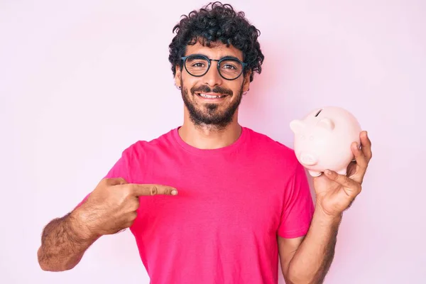 Handsome Young Man Curly Hair Bear Holding Piggy Bank Pointing — Stock Photo, Image