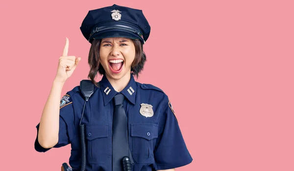 Young beautiful girl wearing police uniform pointing finger up with successful idea. exited and happy. number one.