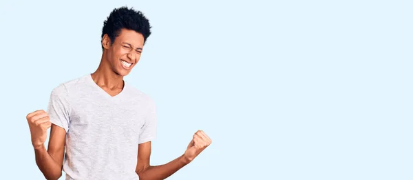 若いアフリカ系アメリカ人の男性は カジュアルな白いTシャツを着て非常に満足し 腕を上げて勝者のジェスチャーを行う興奮し 笑顔と成功のために叫んでいます お祝いのコンセプト — ストック写真