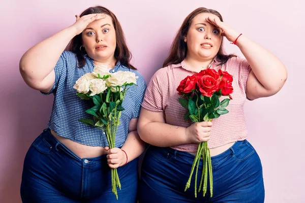 Young plus size twins holding flowers stressed and frustrated with hand on head, surprised and angry face