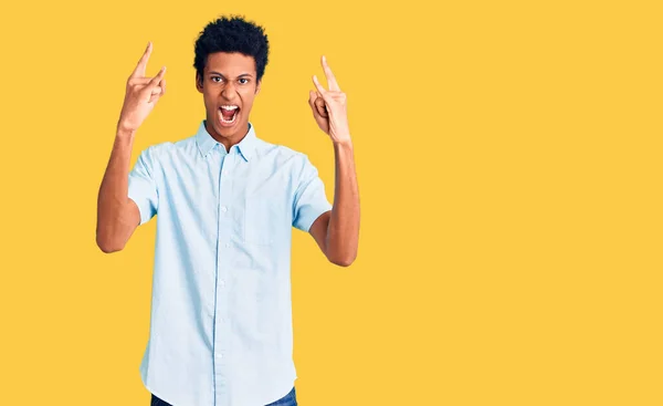 若いアフリカ系アメリカ人の男性が手で岩のシンボルを行う狂気の表現で叫んでカジュアルな服を着ている 音楽スター 重い音楽の概念は — ストック写真