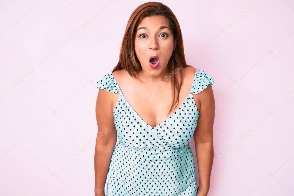 Middle age brunette hispanic woman wearing summer dress scared and amazed with open mouth for surprise, disbelief face 
