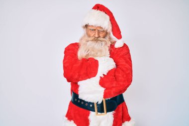Gri saçlı, uzun sakallı, Noel Baba kostümü giyen askılı, kuşkucu ve gergin, yüzünde çapraz kollu tasvip etmeyen bir ifade olan yaşlı adam. negatif kişi. 