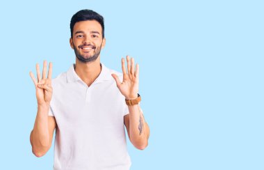 Genç, yakışıklı, günlük kıyafetler giyen, dokuz numaralı parmaklarıyla gösteriş yapan, kendinden emin ve mutlu gülümseyen İspanyol adam.. 