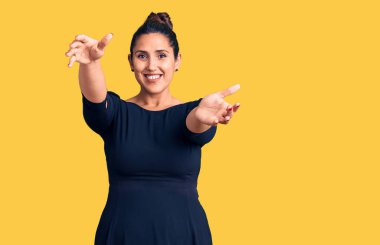 Genç, güzel, esmer, sıradan bir elbise giymiş bir kadın kameraya bakıp sarılmak için kollarını açmış gülümsüyor. Mutluluğu kucaklayan neşeli bir ifade.. 