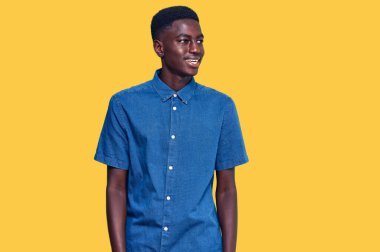 Genç Afro-Amerikan bir adam günlük kıyafetler giyip yüzünde gülümseme, doğal bir ifade ile yan yana bakıyor. Kendinden emin gülen. 