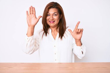 Orta yaşlı esmer, İspanyol iş kadını. Masada oturan ve yedi numaralı parmaklarını göstererek gülümseyen, kendinden emin ve mutlu bir kadın.. 