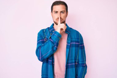 Gündelik kıyafetler giyen genç yakışıklı adam parmakları dudaklarında sessiz olmak istiyor. sessizlik ve gizli konsept. 