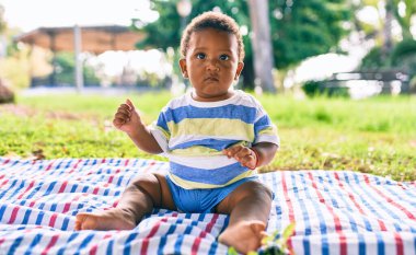 Sevimli Afro-Amerikan çocuk parkta çimlerin üzerinde oturuyor..
