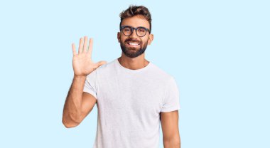 Gündelik kıyafetler giyen ve gözlük takan genç İspanyol adam beş numarayı gösterip işaret ederken kendinden emin ve mutlu gülümsüyor.. 