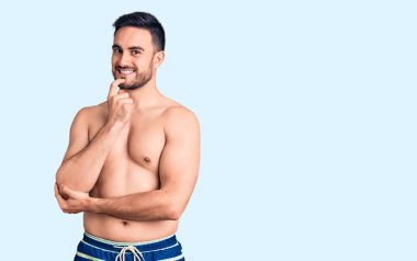 Mayo giyen genç yakışıklı, kameraya kendinden emin bakıyor kollarını kavuşturmuş ve çenesini kaldırmış gülümsüyor. Olumlu düşünmek. 