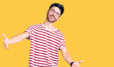 Gündelik giysiler giymiş genç İspanyol adam kameraya bakıp sarılmak için kollarını açmış gülümsüyor. Mutluluğu kucaklayan neşeli bir ifade.. 