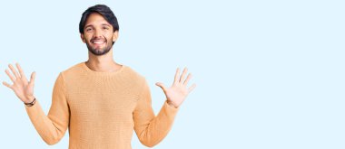 Yakışıklı İspanyol adam gündelik süveter giyer ve parmaklarını on numarayla gösterip gülümserken kendinden emin ve mutlu.. 