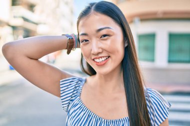 Genç Çinli kadın gülümsüyor. Şehrin caddesinde mutlu bir şekilde yürüyor..