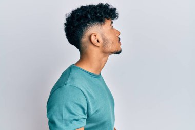 Genç Arap yakışıklı adam günlük giysiler giymiş, rahat bir görünüm takınıyor, kendine güvenen bir gülümsemeyle doğal bir yüz ifadesi takınıyor.. 