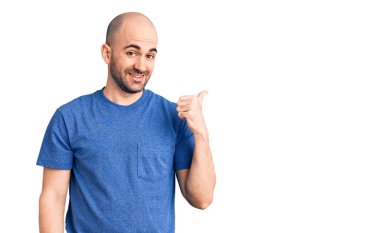 Gündelik tişört giyen genç yakışıklı adam gülümseyen yüz ifadesiyle yan tarafa bakıyor ve başparmağıyla işaret ediyor.. 