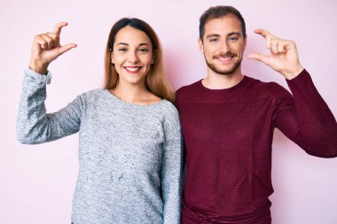Gündelik kıyafetler giyen, gülümseyen, el hareketleriyle el hareketleriyle küçük boy işareti yapan ve kameraya bakan güzel bir çift. ölçüm kavramı. 
