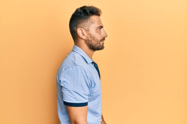 Sakallı, sıradan kıyafetler giyen, rahat bir görünüm takınan, kendine güveni olan yakışıklı bir adam.. 