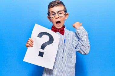 Sevimli sarışın çocuk inek papyonu takıyor ve gözlüklü soru işareti taşıyor başparmağıyla yan tarafı işaret ediyor mutlu bir şekilde ağzı açık gülümsüyor 