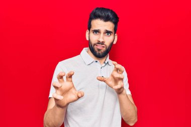 Sakallı, polo gibi iğrenç bir ifade takınan genç yakışıklı bir adam tiksinti tepkisi yüzünden tiksinmiş ve korkmuş bir ifade takınıyor. Eller havada. 