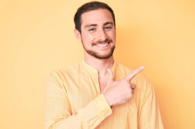 Genç, yakışıklı, günlük kıyafetler giyen, neşeli, yüzünde mutlu ve doğal bir ifadeyle, elleri ve parmaklarıyla işaret eden bir gülümseme olan bir adam. 