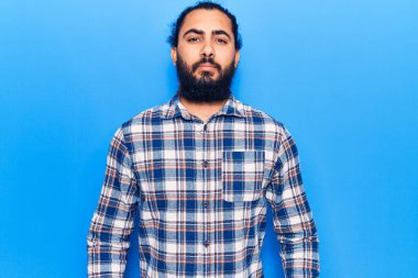 Yüzünde ciddi bir ifade olan gündelik kıyafetler giyen genç bir Arap. Basit ve doğal bir şekilde kameraya bakıyorsun.. 