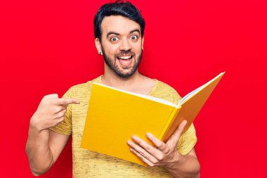 Genç İspanyol adam elinde kitapla gülümsüyor mutlu bir şekilde el ve parmaklarıyla işaret ediyor 