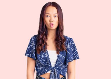 Genç, güzel Çinli kız günlük kıyafetler giyip dudaklarıyla balık suratı yapıyor. Çılgınca ve komik bir jest. Komik ifade. 