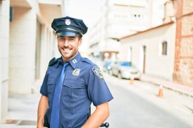 Polis üniforması giyen genç, yakışıklı İspanyol polis mutlu bir şekilde gülümsüyor..