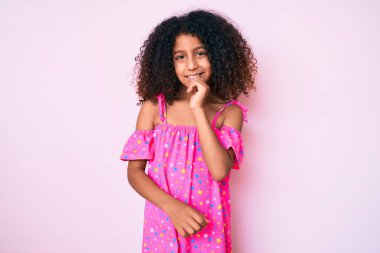 Kıvırcık saçlı Afro-Amerikalı çocuk kameraya kendinden emin bakıyor kollarını kavuşturup gülümsüyor ve çenesini kaldırıyor. Olumlu düşünmek. 