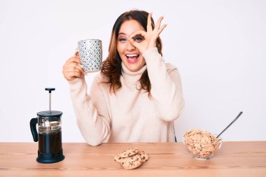 Genç, güzel, beyaz bir kadın masada oturmuş kahvaltısını yaparken mutlu mesut gülümsüyor. 