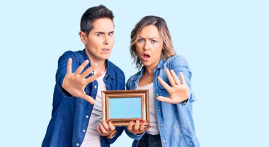 Elinde boş bir çerçeve olan bir çift kadın avuç içi hareketi, kızgın ve hayal kırıklığına uğramış bir ifadeyle durduruyor. 