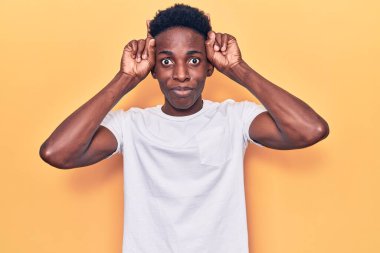 Genç, Afro-Amerikan bir adam, günlük kıyafetler giyip, boynuzları üzerinde parmaklarıyla komik jestler yapıyor. 
