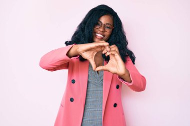 İş ceketi ve gözlük takan güzel Afrikalı bir kadın. Sevgiyle gülümsüyor. Elleriyle kalp sembolü yapıyor. romantik kavram. 