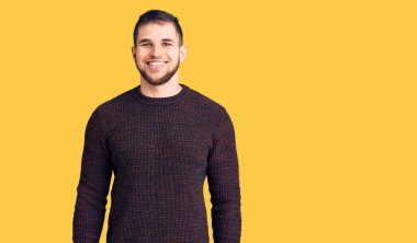 Yüzünde mutlu ve havalı bir gülümseme olan sıradan bir süveter giyen genç yakışıklı bir adam. şanslı kişi. 