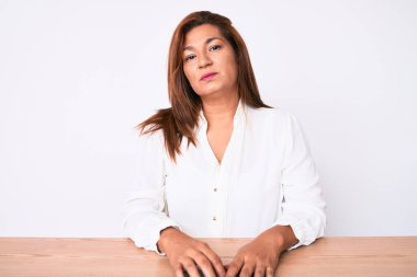 Orta yaşlı esmer, Latin iş kadını. Masada oturan ve yüzünde ciddi bir ifadeyle rahatlamış. Basit ve doğal bir şekilde kameraya bakıyorsun.. 