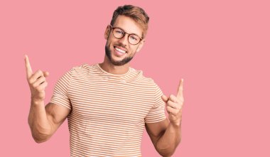 Gündelik kıyafetler giyen ve gözlüklü genç beyaz adam farklı yönleri gösteren kendine güvenen bir şekilde gülümsüyor. reklam için kopyalama alanı 