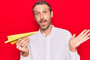 Elinde kağıt uçak tutan genç yakışıklı adam başarıyı mutlu bir gülümsemeyle ve kazanan yüz ifadesiyle kutluyor. 