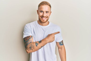 Beyaz bir tişört giyen genç, beyaz bir adam. Gülümsüyor, eli ve parmağı yana doğru uzanıyor. 