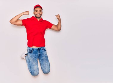 Mutlu gülümseyen üniformalı yakışıklı İspanyol teslimatçı. Yüzünde tebessümle zıplıyor, beyaz arka planda yumruklar havada kutluyor..
