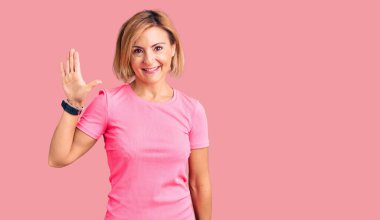 Spor kıyafetleri giyen genç sarışın kadın beş numarayı gösterip işaret ederken kendinden emin ve mutlu bir şekilde gülümsüyor.. 