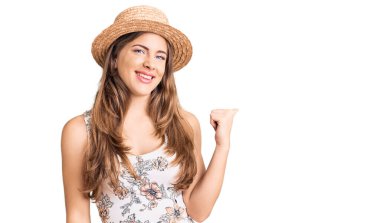 Yazlık şapkalı, gülen yüzlü güzel beyaz kadın başparmağıyla yan tarafa bakıyor ve gülümsüyor.. 