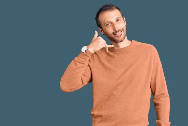 Genç, yakışıklı, sıradan kıyafetler giymiş, gülümseyen, el ve parmaklarıyla telefonla konuşan bir adam. iletişim kavramları. 