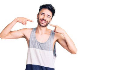 Günlük kıyafetler giyen, neşeli gülümseyen, parmaklarıyla ve ağzıyla işaret eden İspanyol genç bir adam. diş sağlığı kavramı. 